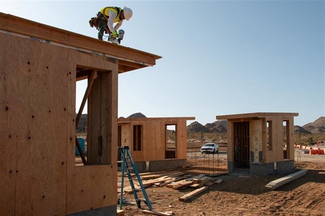 Three small buildings under construction, with a construction worker on the roof of one