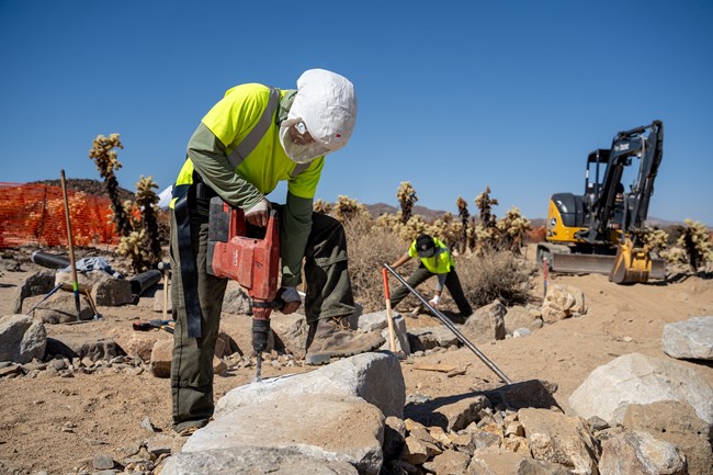 Construction workers drilling into a rock to construct a trail