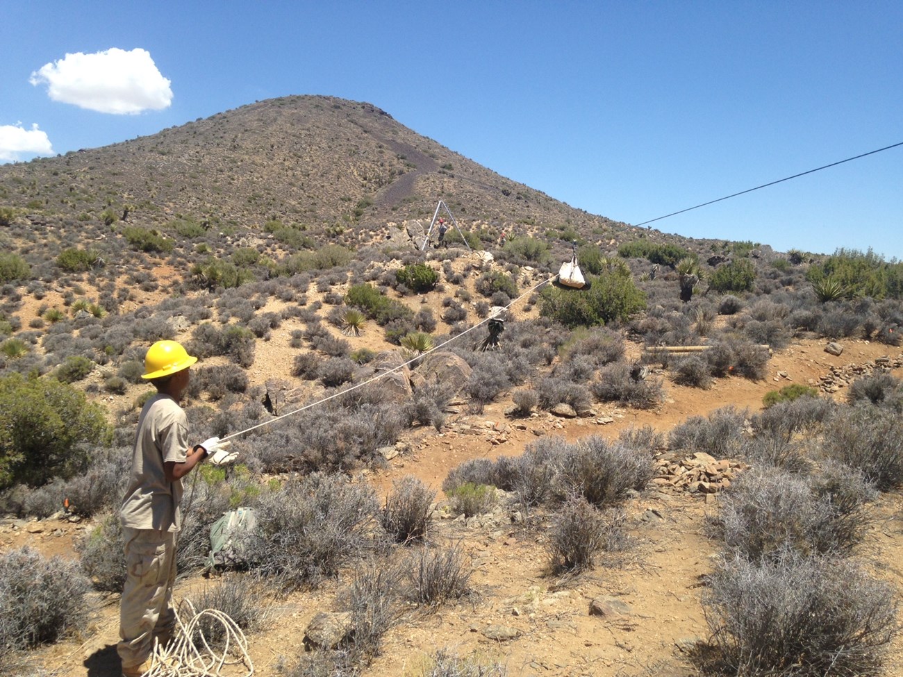 Color photo of a youth conservation corps hire holding the guide rope while using high lining equipment to move materials for trail work. NPS photo