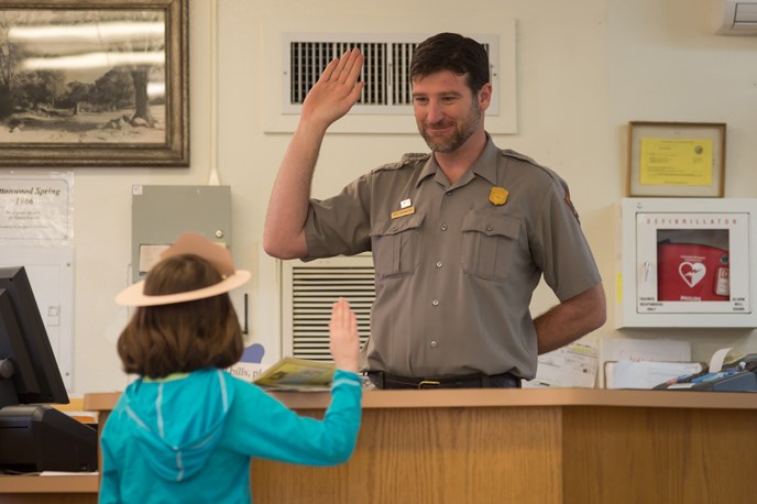 a young girl and a park ranger face each other with right hands raised