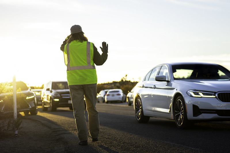 A person with a yellow work vest waves at a vehicle
