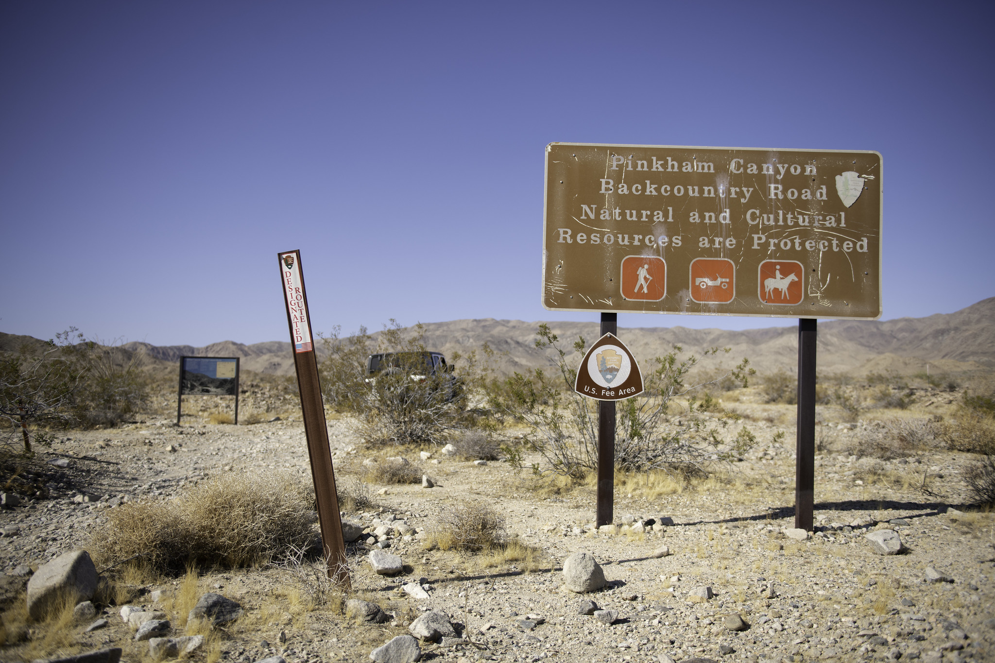 A variety of signs indicating the beginning of Pinkham Canyon Road next to a rocky dirt road.