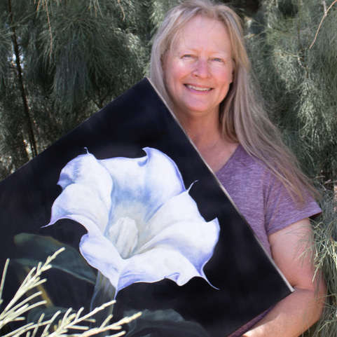 Arist in Residence Marcia Geiger A person smiling and holding up a painting
