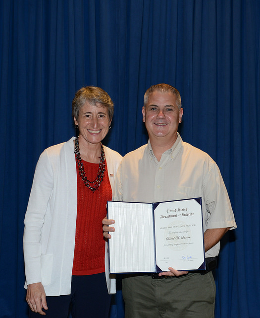 Secretary of the Interior Sally Jewell (left) and Dave Larsen (right) smile together; Larsen hold open an award