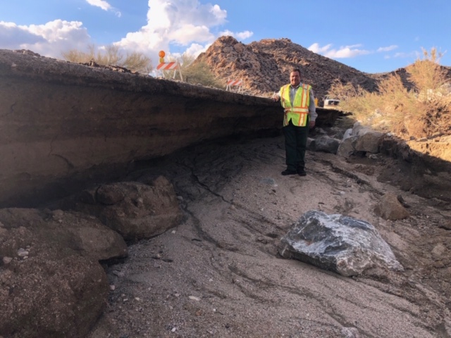 A maintenance worker wearing a high-vis vest stands next to major erosion next to Pinto Basin Road.