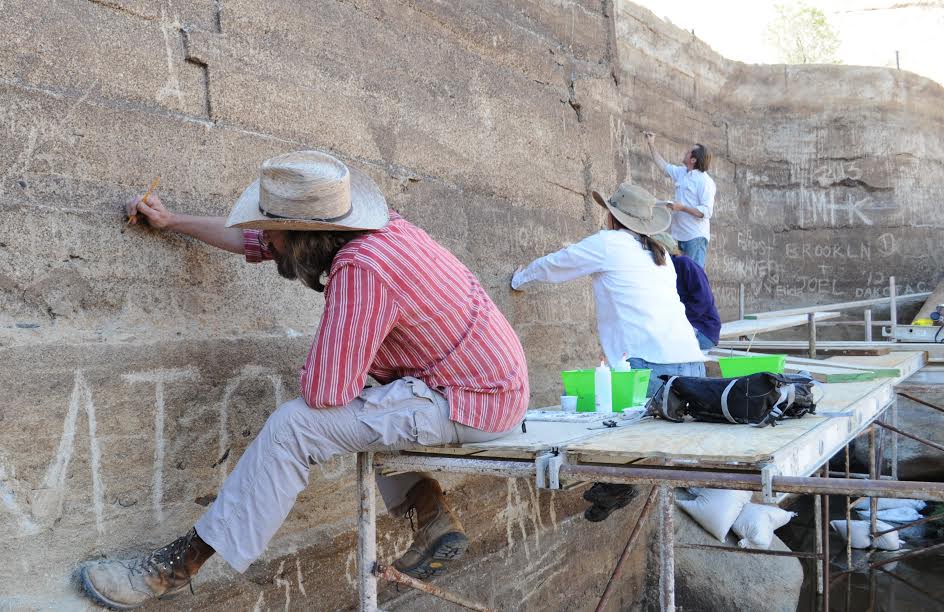 Conservators on scaffolding "in-painting" scratched areas on the dam to match the naturally weathered surface.