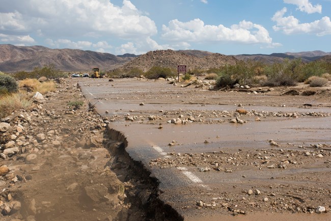 Water and rocks over a road with erosion around the side.