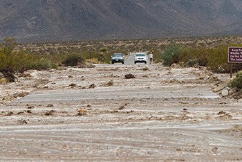 water and debris on a road with two cars stopped in the background.