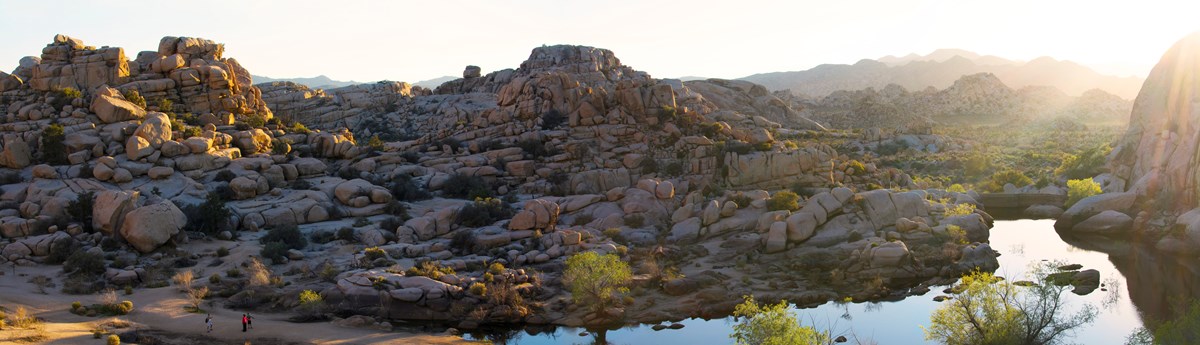 A wide panoramic view of Barker Dam filled with water and surrounded by lush vegetation and rock piles.