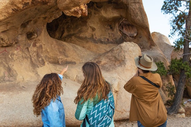 Three women stand at a respectful distance from rock art on a boulder.