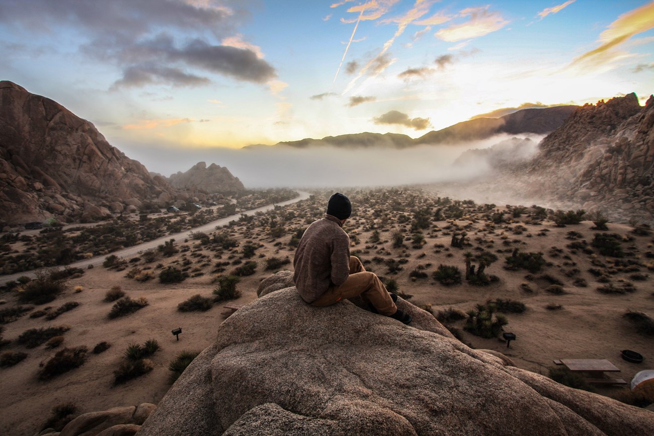 A lone person sits atop a boulder pile as fog fills the background