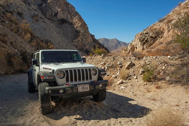 A park vehicle on a sandy road with sloping canyon walls on either side.