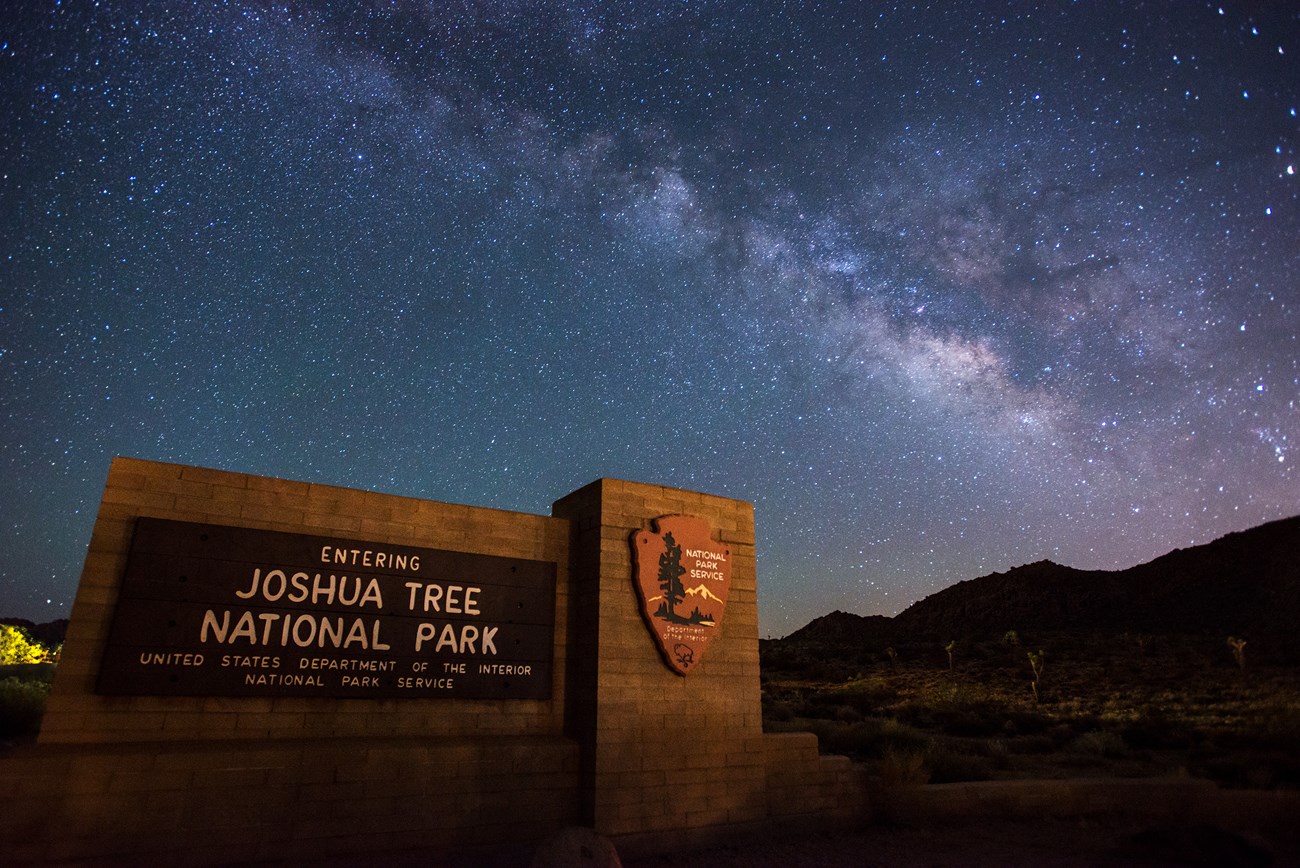 Color photo of brilliant milky way in the sky and the park entrance sign in the front.