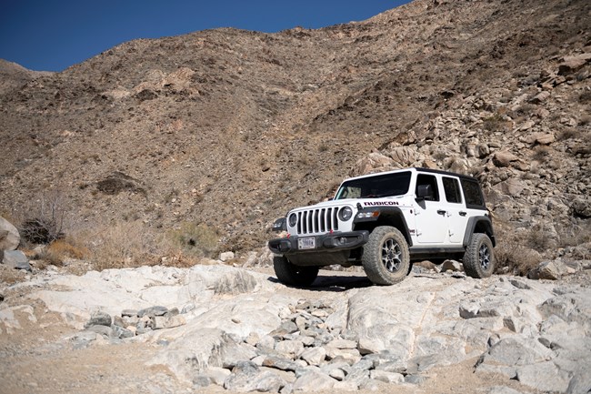 A Jeep crawls down a rocky slope in the middle of a desert wash on a designated route.