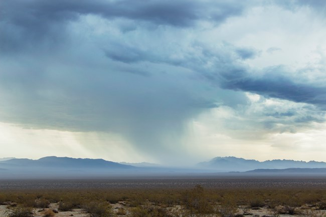 Rain cloud drops rain on a desert valley with mountains in the distance