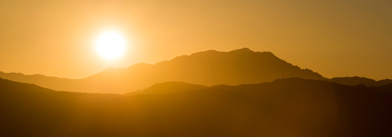 The sun setting over silhouetted mountains.