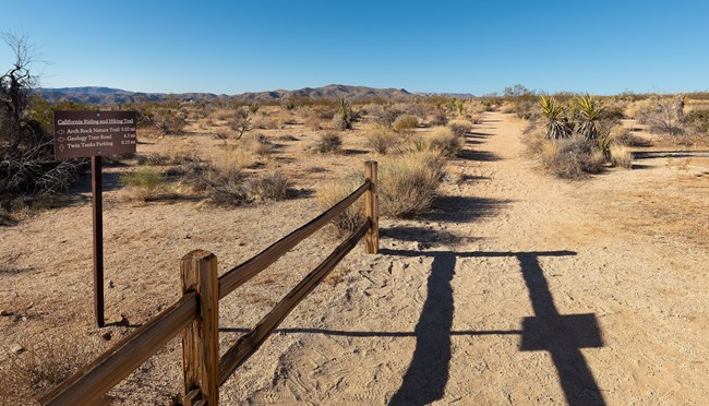 a trail sign with desert vegetation and mountains in the background