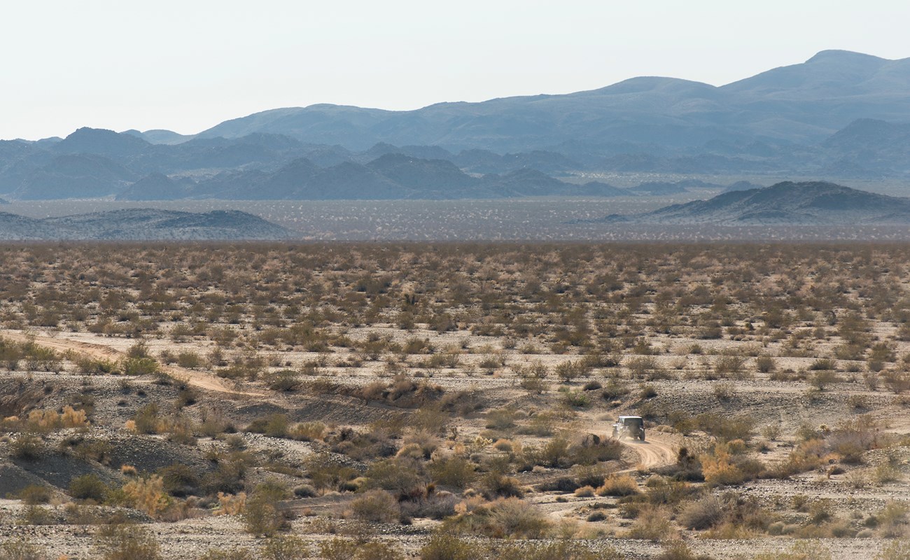 Color photo of a 4-wheel drive vehicle on a backcountry road through the desert. NPS / Brad Sutton