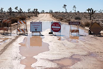 Signs and saw horses closing a road, signs say "Authorized Vehicles Only", "Do Not Enter", "Closed", and "Flooded"