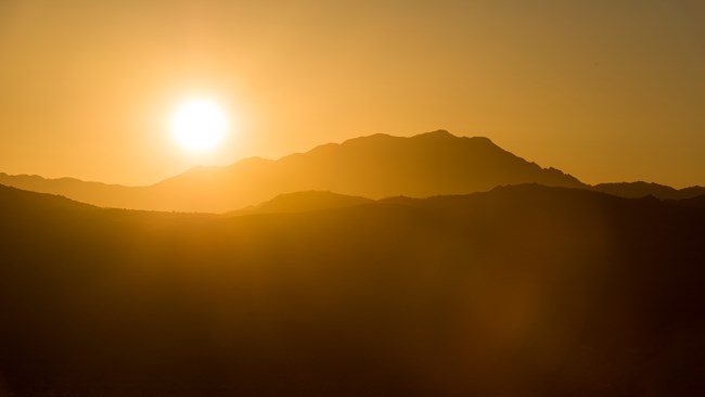 The sun sets over dark mountains