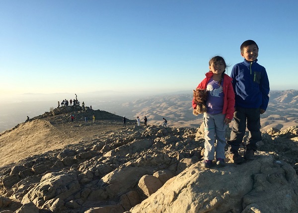 Two kids stand at a rocky peak above hills in the distance. Two kids stand at a rocky peak above hills in the distance.