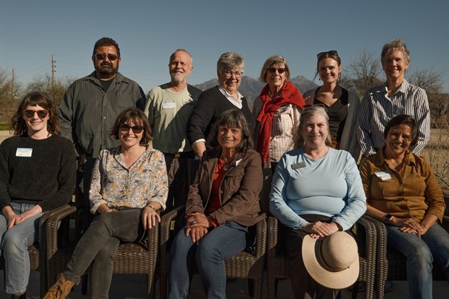 A group of people wearing hats and sunglasses stand and sit next to each other outside for a photo