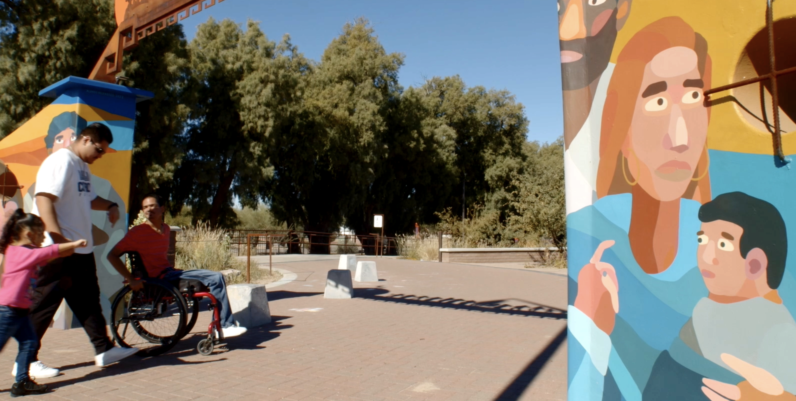 ATCHP accessible space A man in a wheelchair and his friends enter a park through a colorful archway with a mural of a family