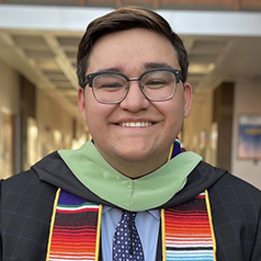 A person with cropped brown hair and glasses smiles wearing an ASU graduation sash