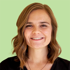 A person wearing a black shirt with shoulder length blond hair smiles in front of a light green background