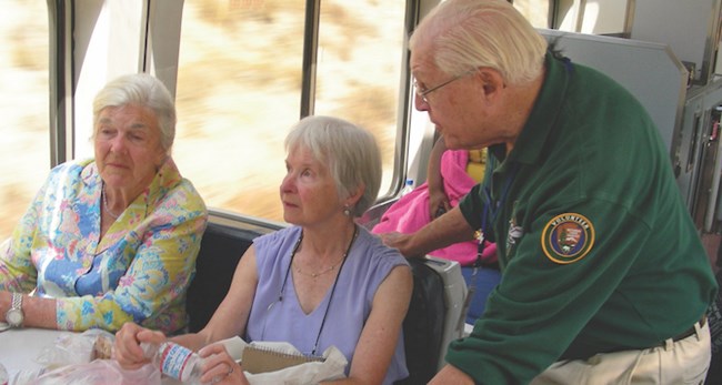 A NPS volunteer talks to a riders on a train