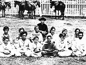 A black and white photo of a man in black, Father Damien and many children.