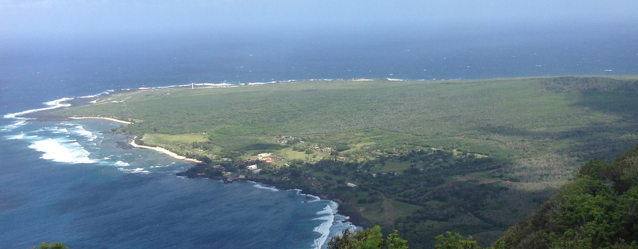 View looking down on a prominent green peninsula surrounded by water. Some buildings are visible.