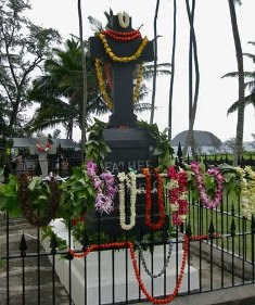 A grave with a large cross statue and many leis decorating it.