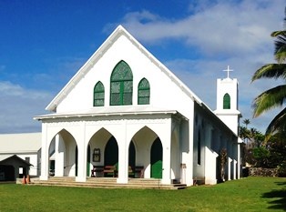 A tall white church building with a steeple and large windows surrounded by a lawn.