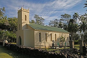 A large light-colored church building with many windows and a rock wall running in front of the building.