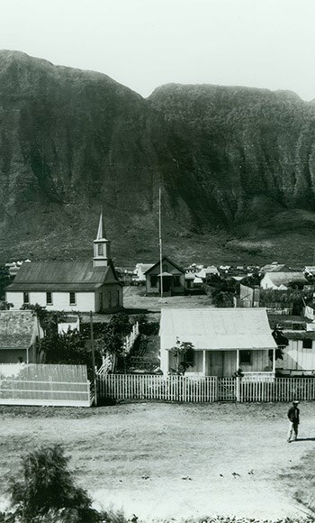 The cliffs of Molokai rising behind flat land with buildings