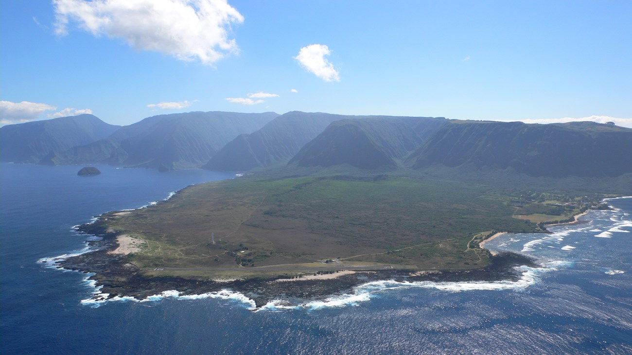 An aerial view of the Kalaupapa peninsula surrounded by ocean on three sides and large cliffs in the background