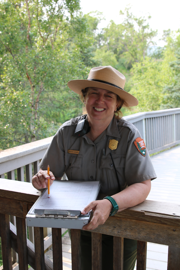 Chris staffing the Treehouse at Brooks Falls park ranger holding clipboard, smiling