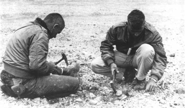  Two men sit on the ground and hammer rocks