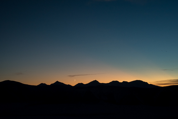 A sliver moon setting behind mountain silhouette