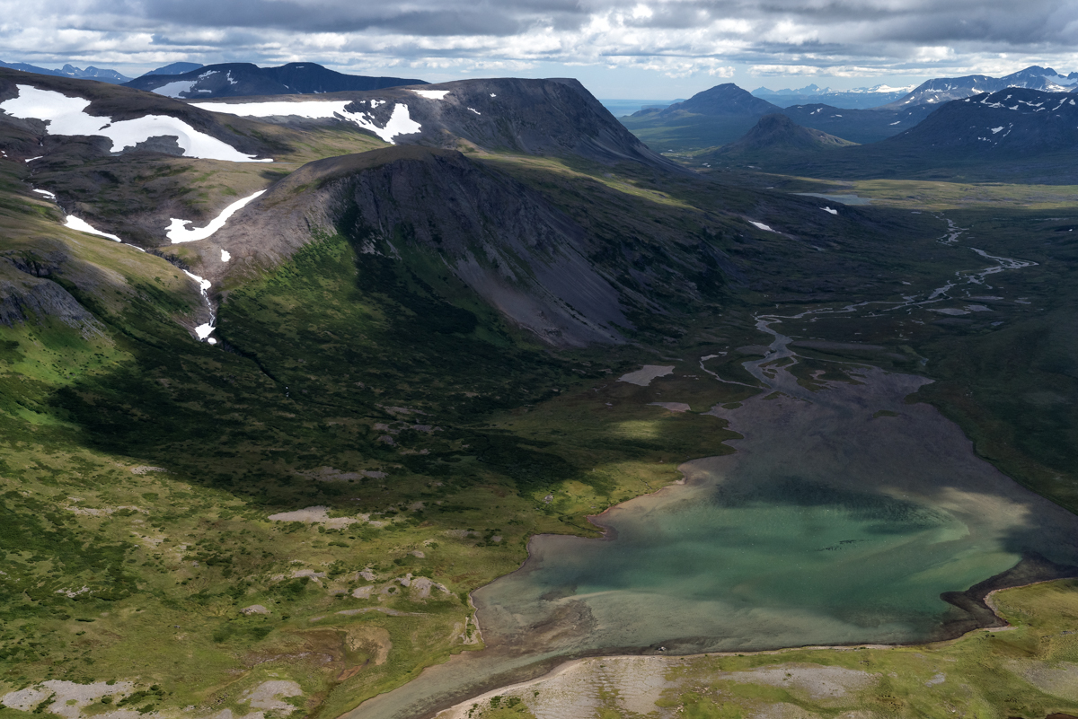 Aerial view of a green lake and snow covered mountains