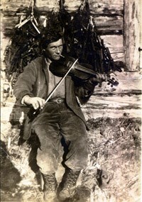 Roy Fure poses with his fiddle outside of his cabin in Bay of Islands.