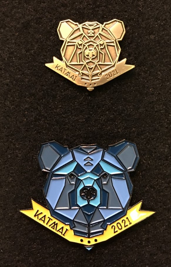 2021 Bear pin Bronze pin of a bear head with the words Katmai 2021 (above), blue bear head with the words Katmai 2021 below.