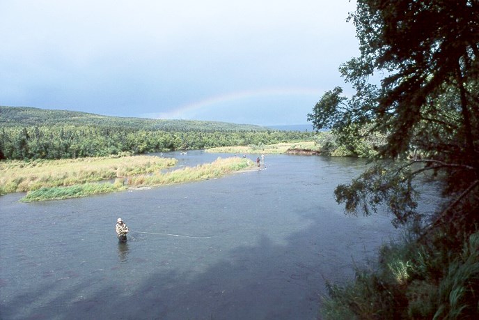 angler stands in river with rainbow on horizon