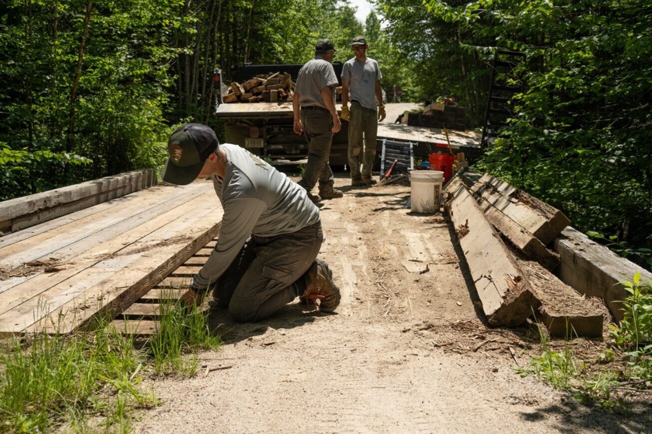 Three NPS roads crew fix a wooden bridge.
