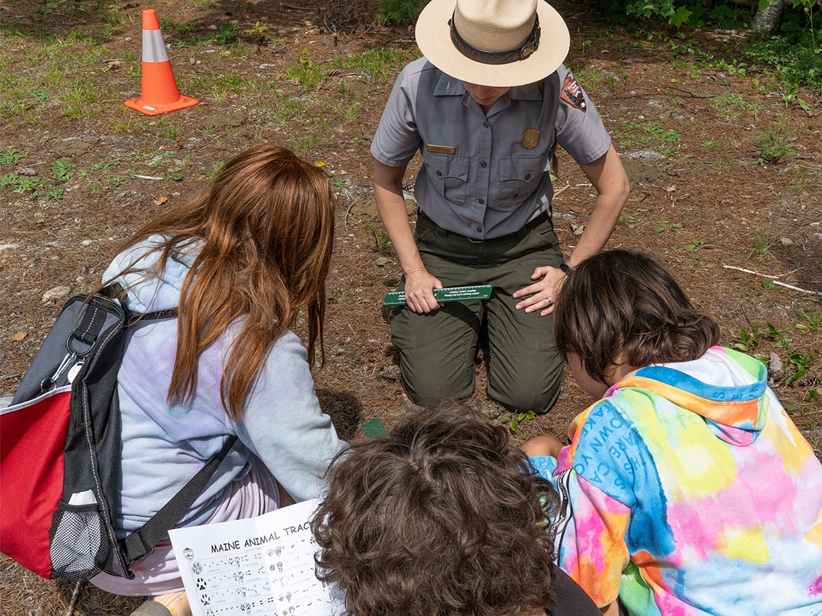 A NPS ranger teaches a group of students about animal tracks at the national monument on a sunny day.