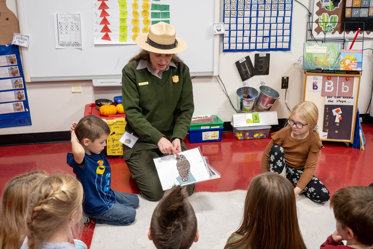 A NPS ranger in uniform engages with a group of student during a program about nocturnal animals inside a school classroom.