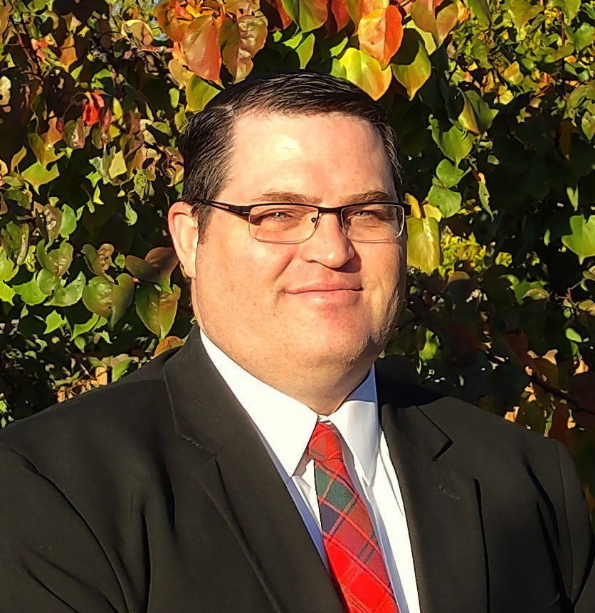A man in a suit in front of a bush or tree