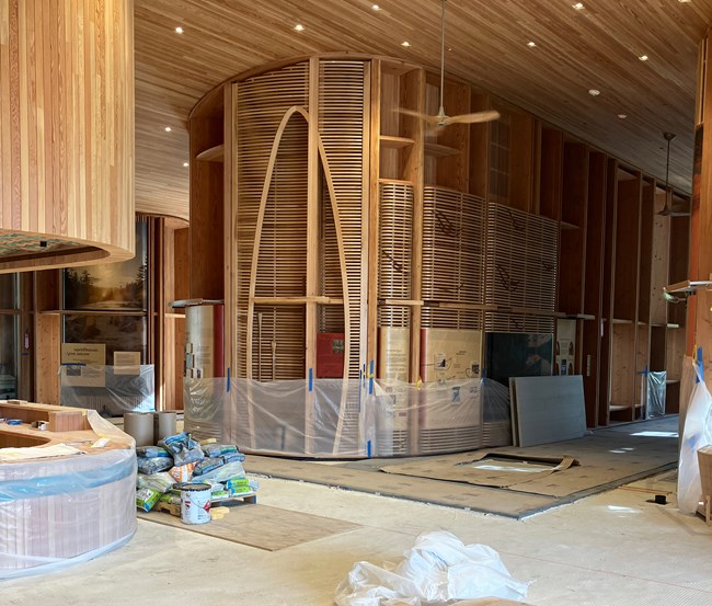 Interior of Tekαkαpimək Contact Station during construction. On the left is a curved portion of the information desk. To the right some exhibits are visible though they are partially covered by plastic during the installation of the floor.