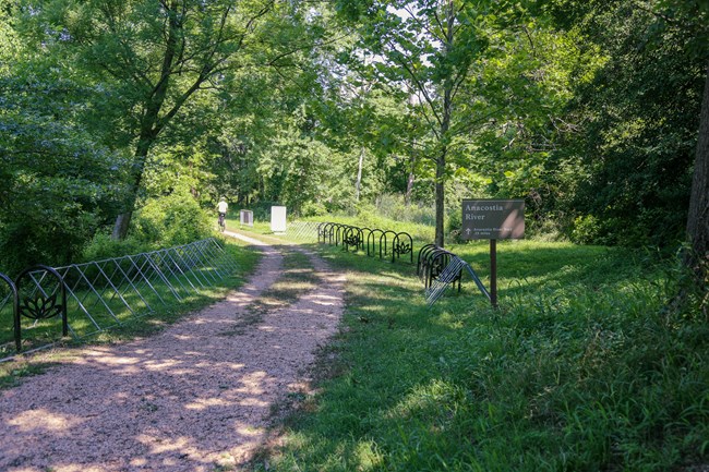 A dirt and gravel trail lined with bike racks leads through a grassy wooded area.